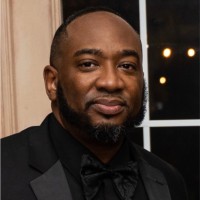 Man in a black tuxedo and bow tie, smiling at the camera (head-and-shoulders portrait).