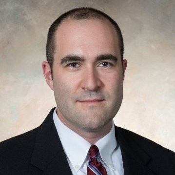 Professional head-and-shoulders portrait of a man in a dark suit, white shirt, and red striped tie against a neutral backdrop.