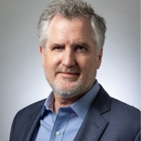 Professional head-and-shoulders portrait of a middle-aged man in a blue suit and light blue shirt against a neutral background.