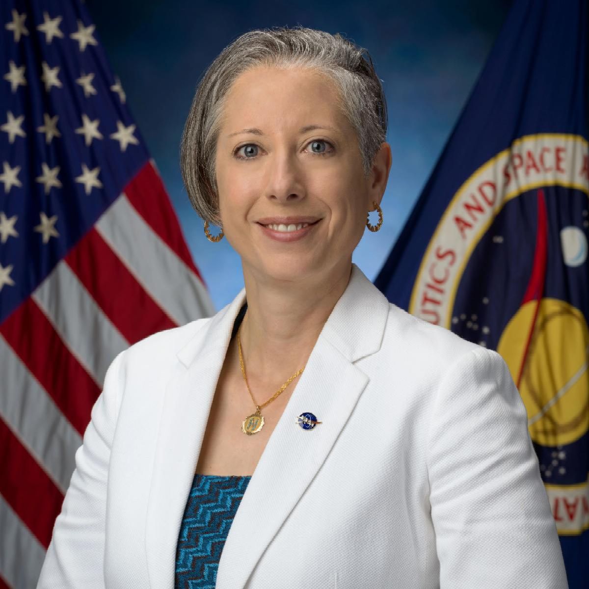 Portrait of a smiling woman in a white blazer with the American flag and a space agency flag in the background.