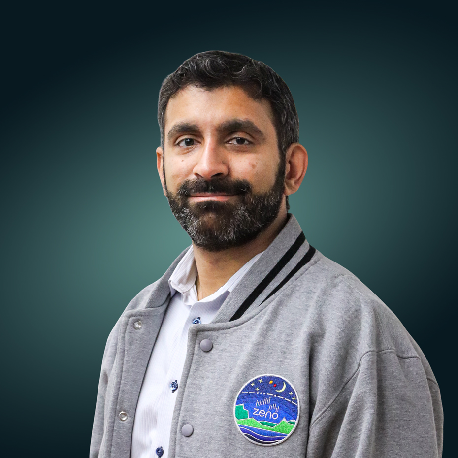 Head-and-shoulders portrait of a man with a beard in a gray varsity jacket with a circular badge, against a teal gradient background.