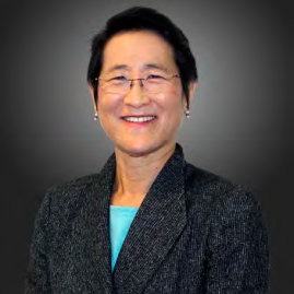 Smiling Asian woman in a dark blazer and turquoise top, professional headshot against a gray gradient background.